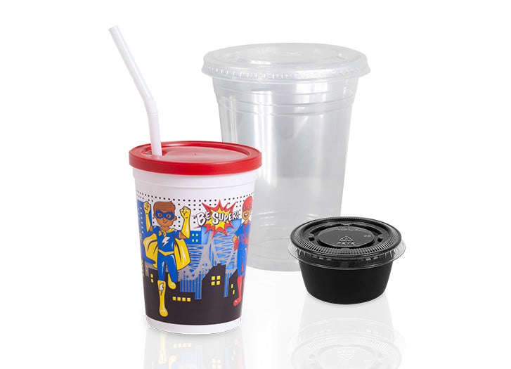 A plastic cup with a red lid and straw, featuring cartoon superheroes, sits beside a clear plastic cup with a lid and a small black sauce container with a black lid.