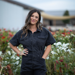 Nikki, founder of Lovely Hollow flower farm, standing in her field of colorful zinnias and sunflowers