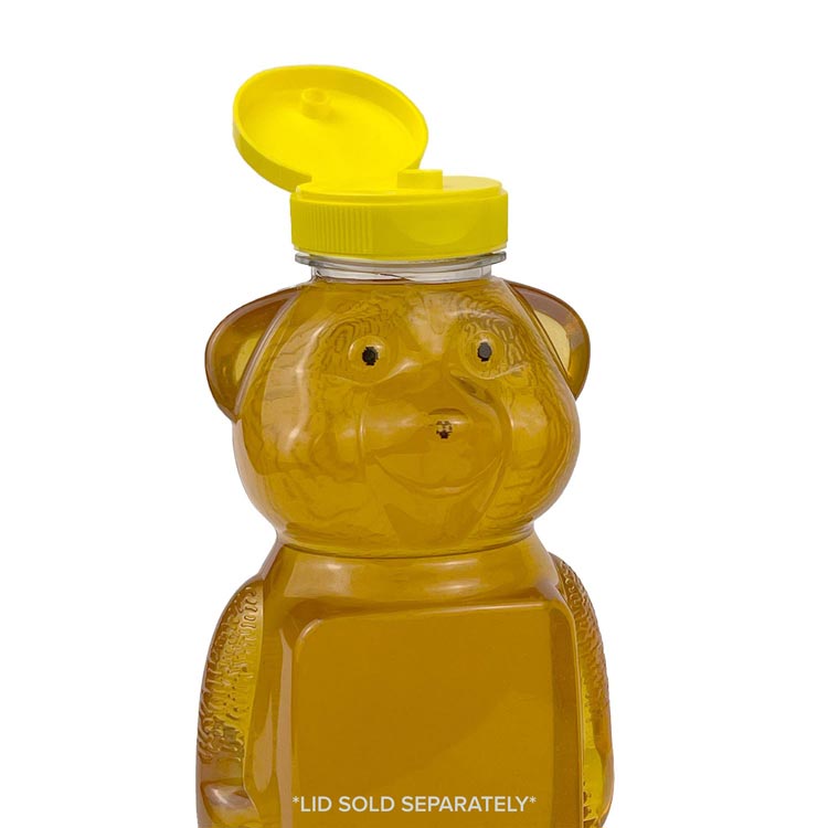 A clear plastic honey bear bottle filled with honey features a yellow flip-top lid. Text at the bottom reads, “LID SOLD SEPARATELY.” The lid is open and the bear is facing forward.