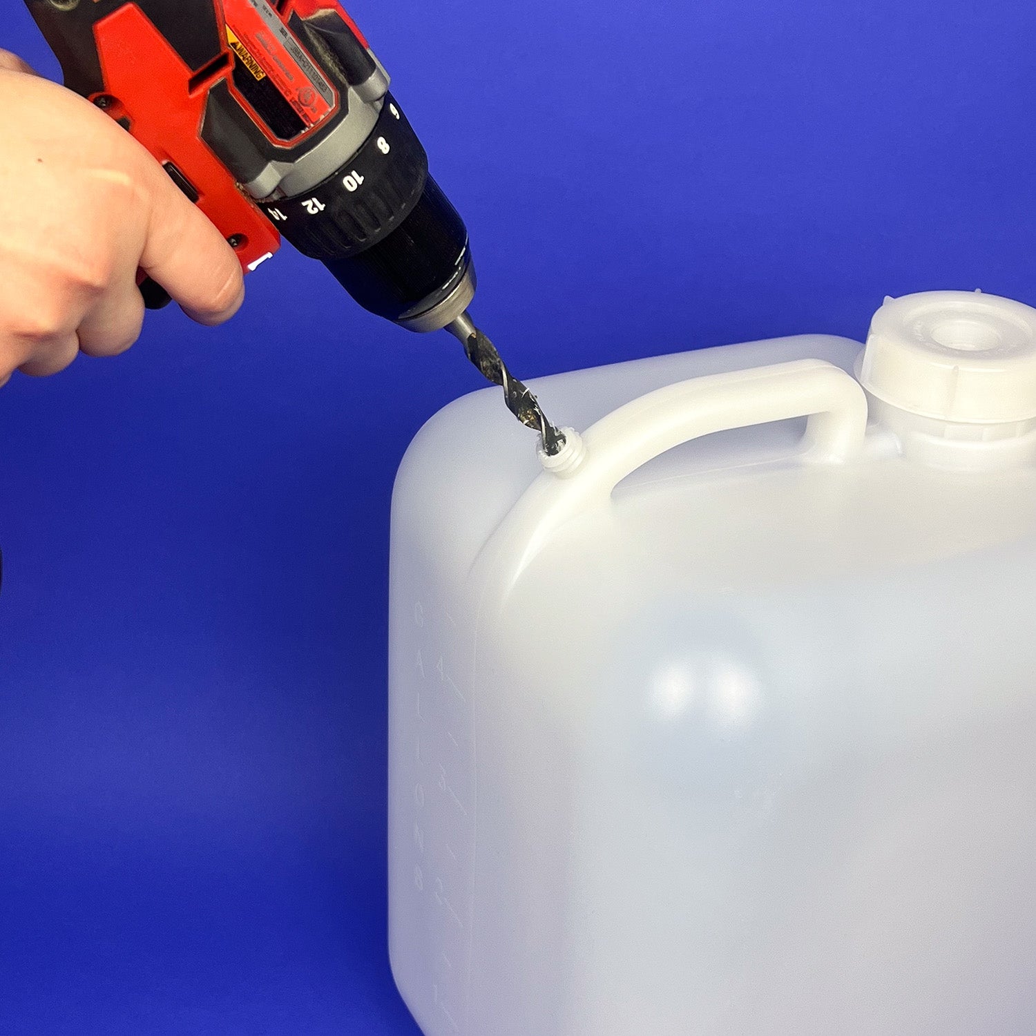 A person uses a power drill to make a hole near the handle of a 5 Gallon BPA-Free Food-Grade Hedpak with 70 mm Cap, a large white plastic container, against a blue background.