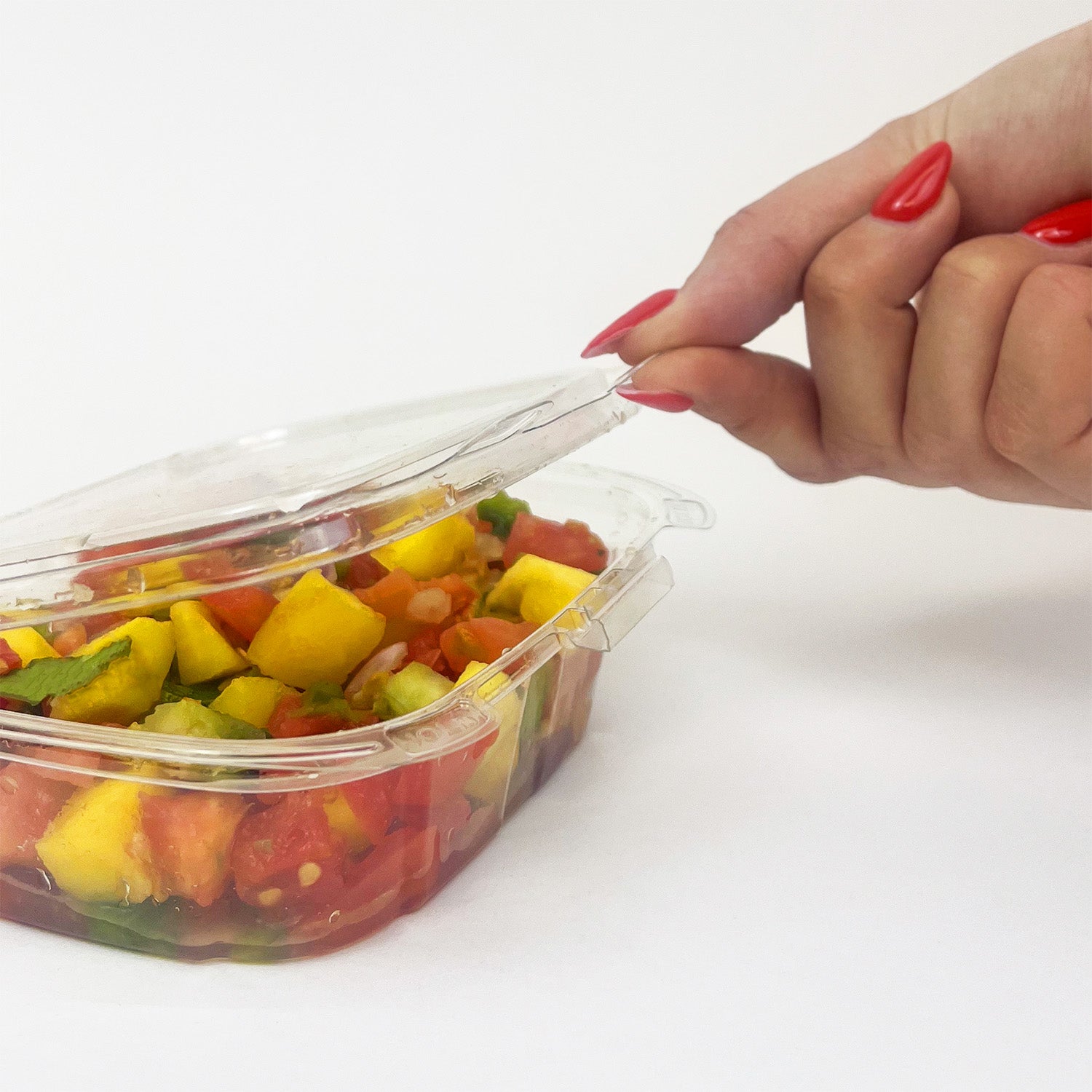A hand with red painted nails opens an 8 oz. Tamper-Evident Crystal Seal Container filled with a colorful salad featuring mango, tomato, and green veggies, displayed on a white background. Case contains 210 containers.
